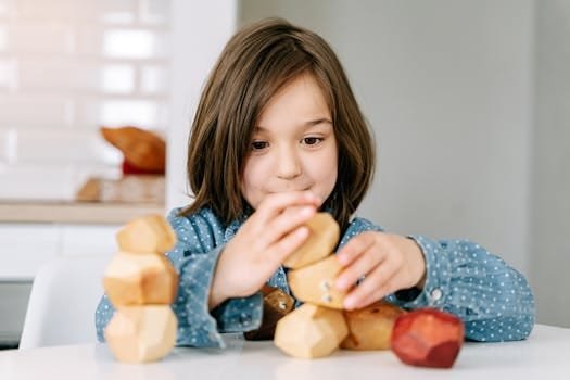 Child playing with wooden blocks indoors, focusing on playful and educational activity.